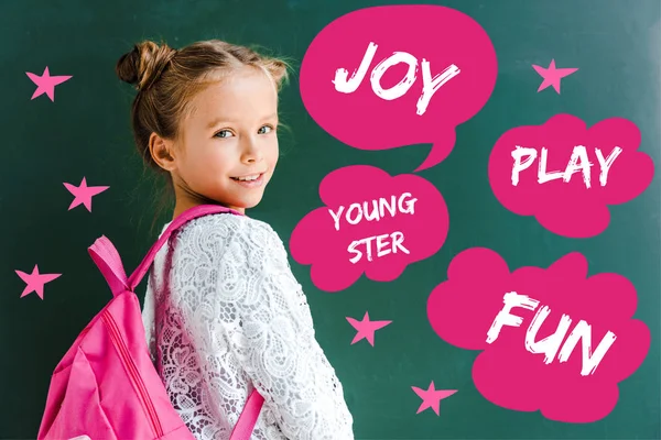 Happy schoolkid smiling while standing with backpack near speech bubble and thought bubbles with words on green — Stock Photo