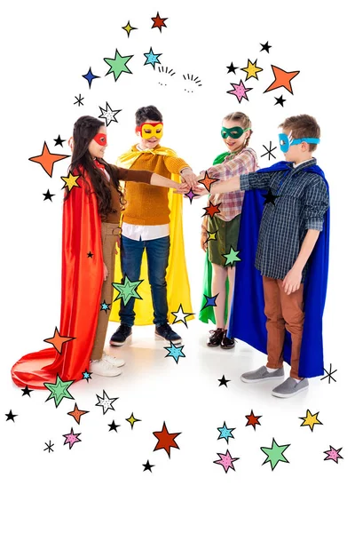 Happy kids in superhero costumes and masks stacking hands near stars on white — Stock Photo