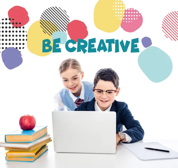 Glückliche Schulkinder mit Laptop am Schreibtisch mit Büchern in der Nähe kreative Buchstaben auf weiß — Stockfoto