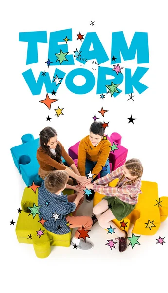 High angle view of kids sitting on jigsaw puzzle poufs and stacking hands near teamwork lettering on white — Stock Photo
