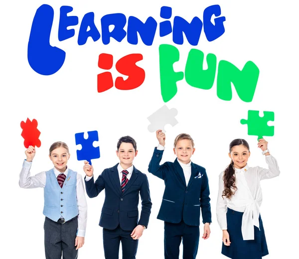 Happy kids in formal wear holding puzzle pieces near learning is fun lettering on white — Stock Photo