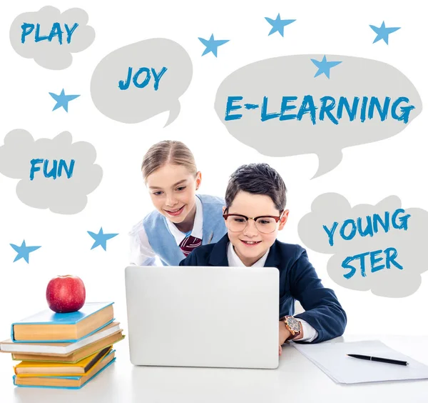 Happy schoolchildren using laptop at desk with books near speech bubbles with lettering on white — Stock Photo