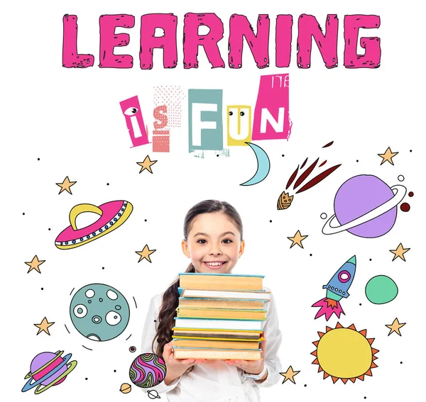 Smiling schoolgirl holding books and looking at camera near learning is fun letters on white — Stock Photo