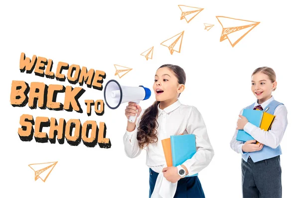 Schoolgirls in formal wear holding books and shouting in megaphone near welcome back to school letters on white — Stock Photo