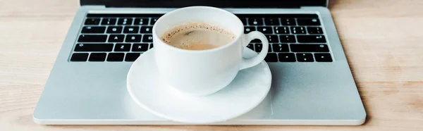 Panoramic shot of cup of coffee on laptop in office — Stock Photo