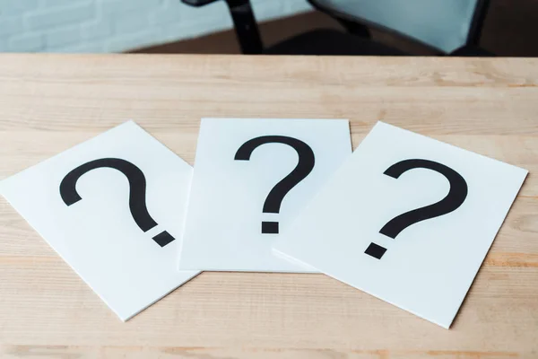 Black question marks on white papers on wooden table — Stock Photo