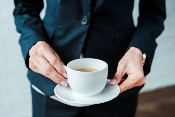 Обрезанный вид женщины, держащей чашку кофе и блюдце в офисе — стоковое фото