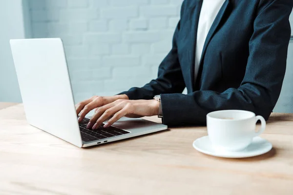 Selektiver Fokus der Geschäftsfrau, die auf Laptop neben Tasse mit Kaffee tippt — Stockfoto