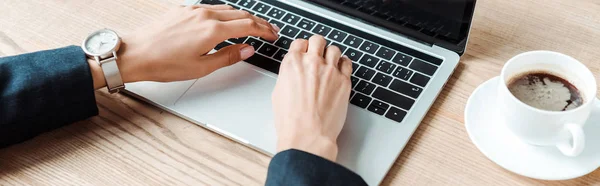 Tiro panorâmico de empresária digitando no laptop perto da xícara com café na mesa — Fotografia de Stock