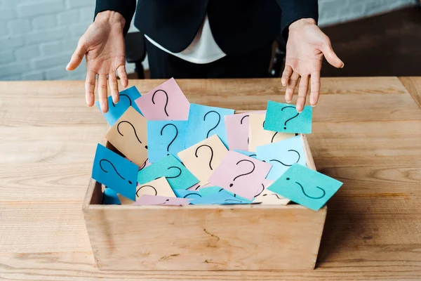 Cropped view of woman gesturing near box with question marks on sticky notes — Stock Photo