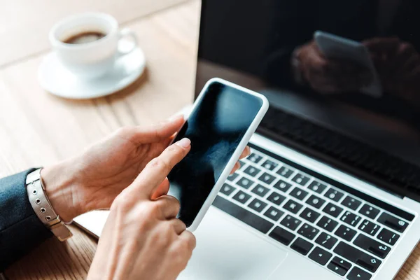 Vista ritagliata della donna che punta con il dito allo smartphone con schermo vuoto vicino al computer portatile — Foto stock