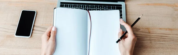 Панорамний постріл Жінка тримає блокнот поблизу ноутбука і смартфона — стокове фото