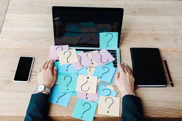 Vista ritagliata di donna vicino note appiccicose con punti interrogativi sul computer portatile — Foto stock