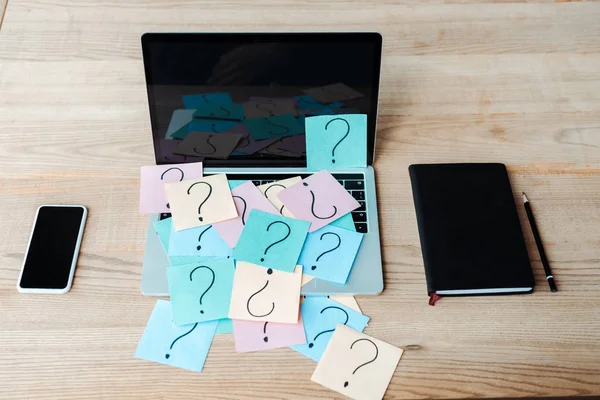 Overhead view of sticky notes with question marks on laptop near notebook and smartphone — Stock Photo