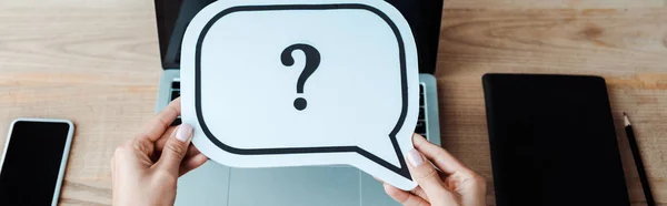 Panoramic shot of woman holding speech bubble with question mark near laptop with blank screen — Stock Photo