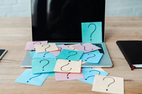 Selective focus of sticky notes with question marks on laptop with blank screen near notebook — Stock Photo