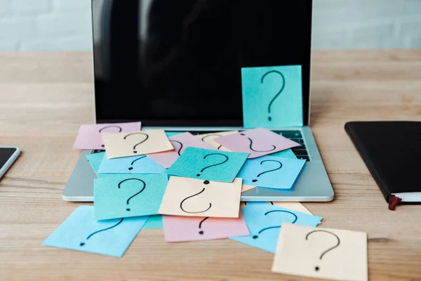 Selektive Fokussierung von Haftnotizen mit Fragezeichen auf Laptop mit leerem Bildschirm in der Nähe des Notebooks — Stockfoto