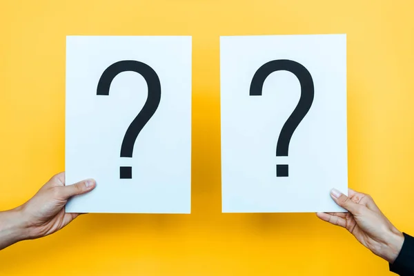 Cropped view of woman and man holding blanks with question marks on orange — Stock Photo