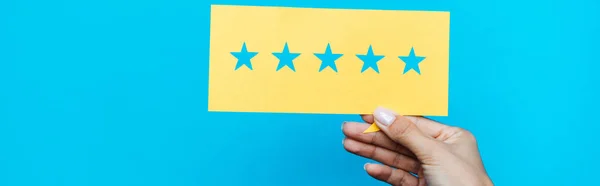 Panoramic shot of woman holding yellow paper with stars isolated on blue — Stock Photo