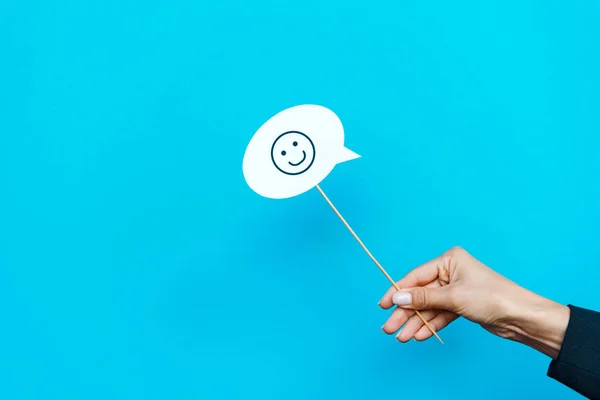 KYIV, UKRAINE - AUGUST 5, 2019: cropped view of woman holding stick with happy face on blue — Stock Photo