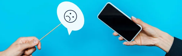 KYIV, UKRAINE - AUGUST 5, 2019: panoramic shot of woman holding stick with sad face near man holding smartphone with blank screen on blue — Stock Photo