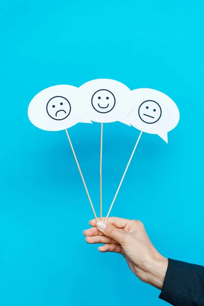 KYIV, UKRAINE - AUGUST 5, 2019: cropped view of woman holding set with emoticons on speech bubbles and sticks on blue — Stock Photo