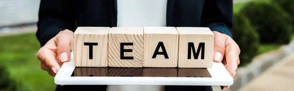 Panoramic shot of woman holding digital tablet and wooden cubes with team letters — Stock Photo