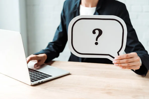 Cropped view of woman holding speech bubble with question mark while working in office — Stock Photo