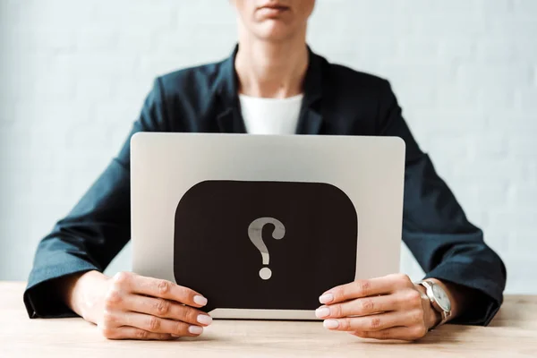 Vue recadrée d'une femme tenant une bulle d'expression noire avec un point d'interrogation alors qu'elle est assise au bureau — Photo de stock