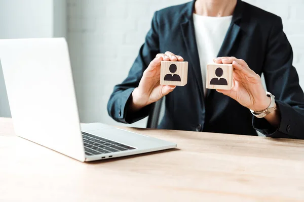 Cropped view of businesswoman holding wooden cubes with human shapes near laptop — Stock Photo