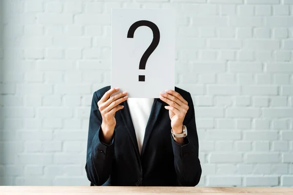 Cropped view of woman covering face while holding placard with question mark near brick wall — Stock Photo