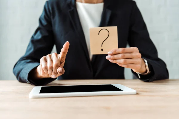 Cropped view of woman holding sticky note with question mark near digital tablet while pointing with finger — Stock Photo