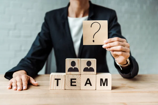 Cropped view of woman holding sticky note with question mark near wooden cubes — Stock Photo