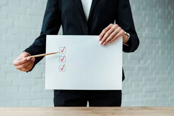 Cropped view of woman holding pencil near paper with check list — Stock Photo