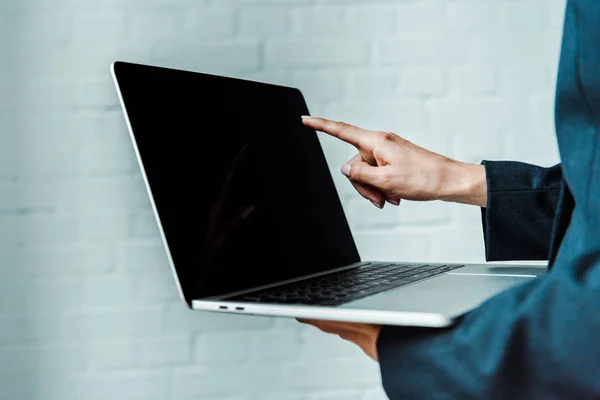 Cropped view of woman pointing with finger at laptop with blank screen — Stock Photo