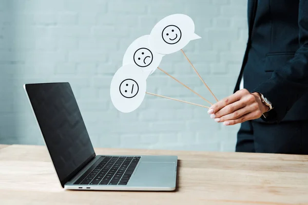 KYIV, UKRAINE - AUGUST 5, 2019: cropped view of woman holding sticks with set of emotions near laptop — Stock Photo