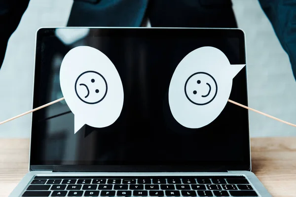 KYIV, UKRAINE - AUGUST 5, 2019: cropped view of woman holding sticks with sad and happy emotions near laptop with blank screen — Stock Photo