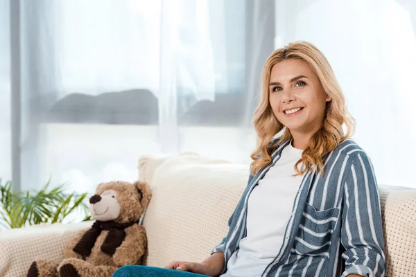 Happy woman sitting on sofa near soft toy — Stock Photo