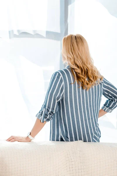 Visão traseira da mulher loira de pé com a mão no quadril em casa — Fotografia de Stock