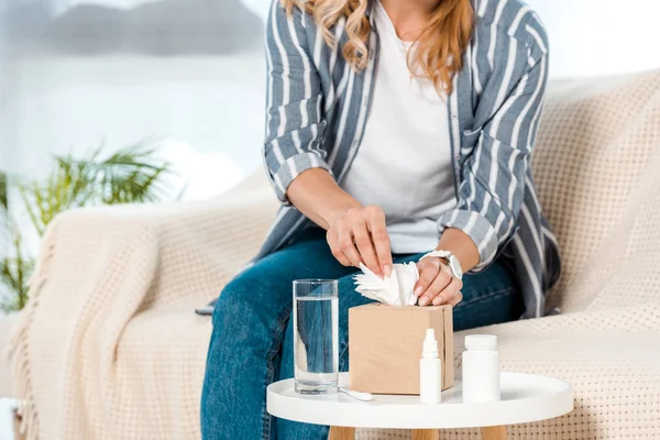 Vue recadrée d'une femme malade assise sur un canapé et prenant une serviette près d'un verre d'eau — Photo de stock