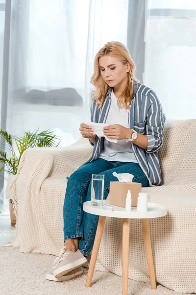 Sick woman sitting on sofa and holding napkin near glass with water — Stock Photo