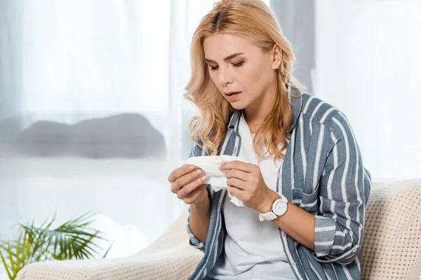 Sick woman sitting on sofa and looking at napkin — Stock Photo