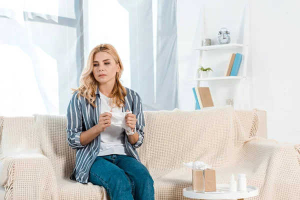 Mujer enferma sentada en el sofá con cerca de caja de pañuelos en la mesa - foto de stock