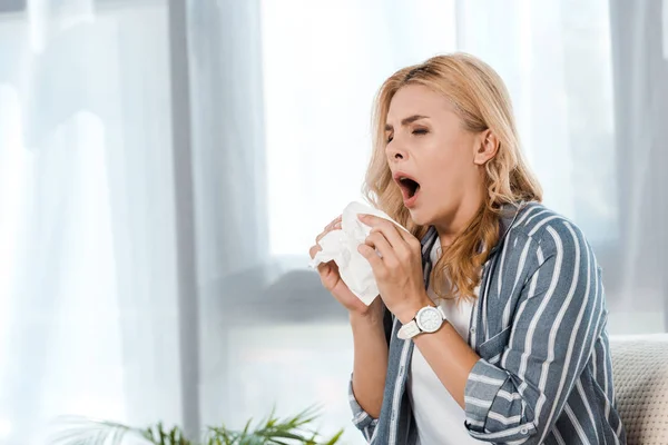 Woman with closed eyes holding napkin and sneezing at home — Stock Photo