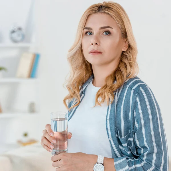 Sad woman looking at camera while holding glass with water — Stock Photo