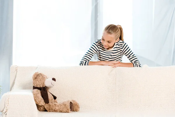 Glückliches Kind schaut Teddybär auf Sofa an — Stockfoto