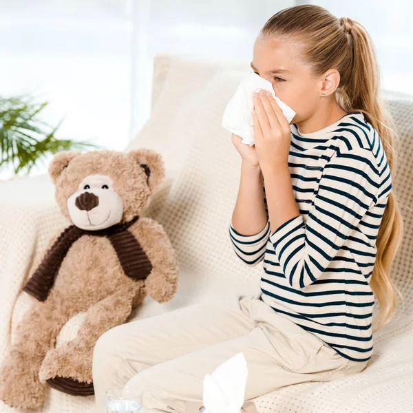 Diseased kid sneezing in tissue neat teddy bear — Stock Photo