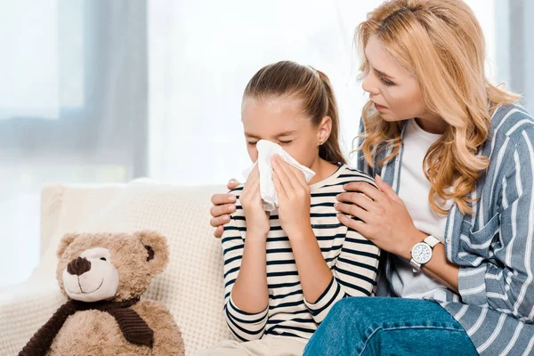 Frau sitzt neben Tochter und niest in Gewebe neben Teddybär — Stockfoto