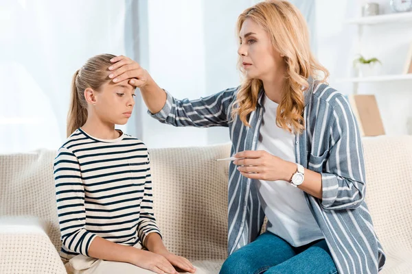 Besorgte Mutter berührt Stirn ihrer Tochter im Wohnzimmer — Stockfoto
