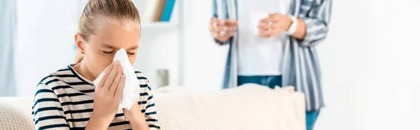 Panoramic shot of kid with closed eyes sneezing near mother at home — Stock Photo